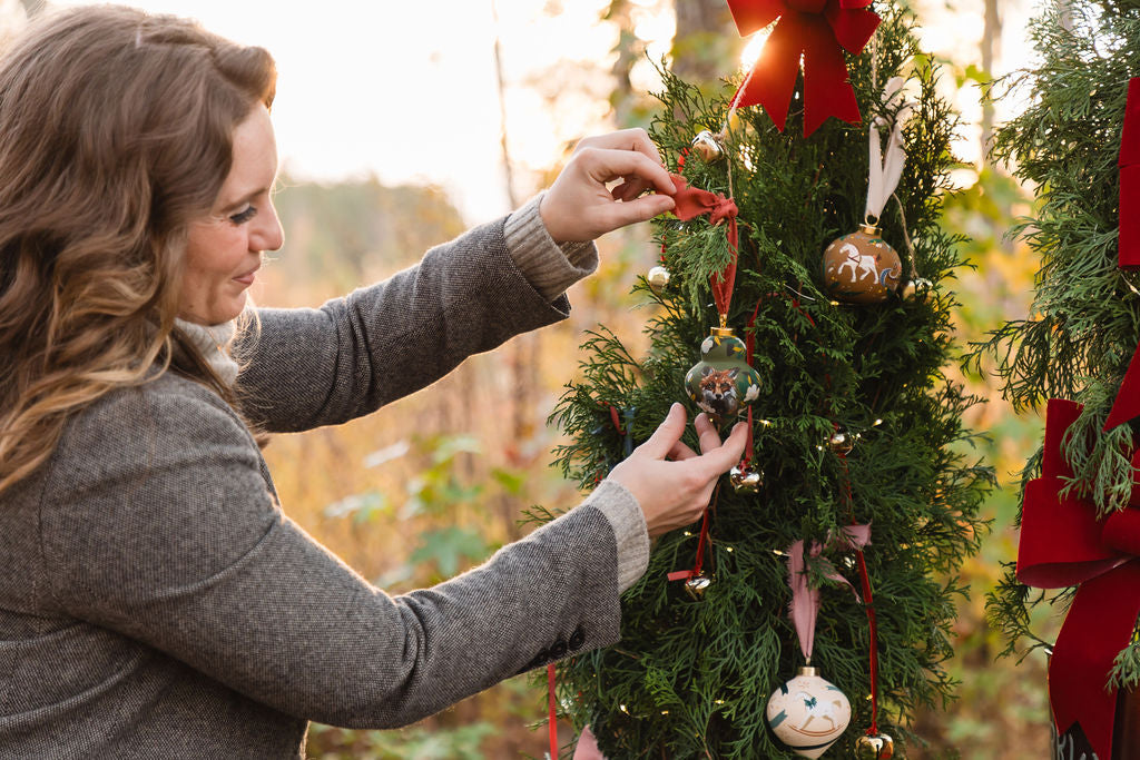 Artist Larissa Ann hanging her hand-painted porcelain ornaments on a Christmas tree