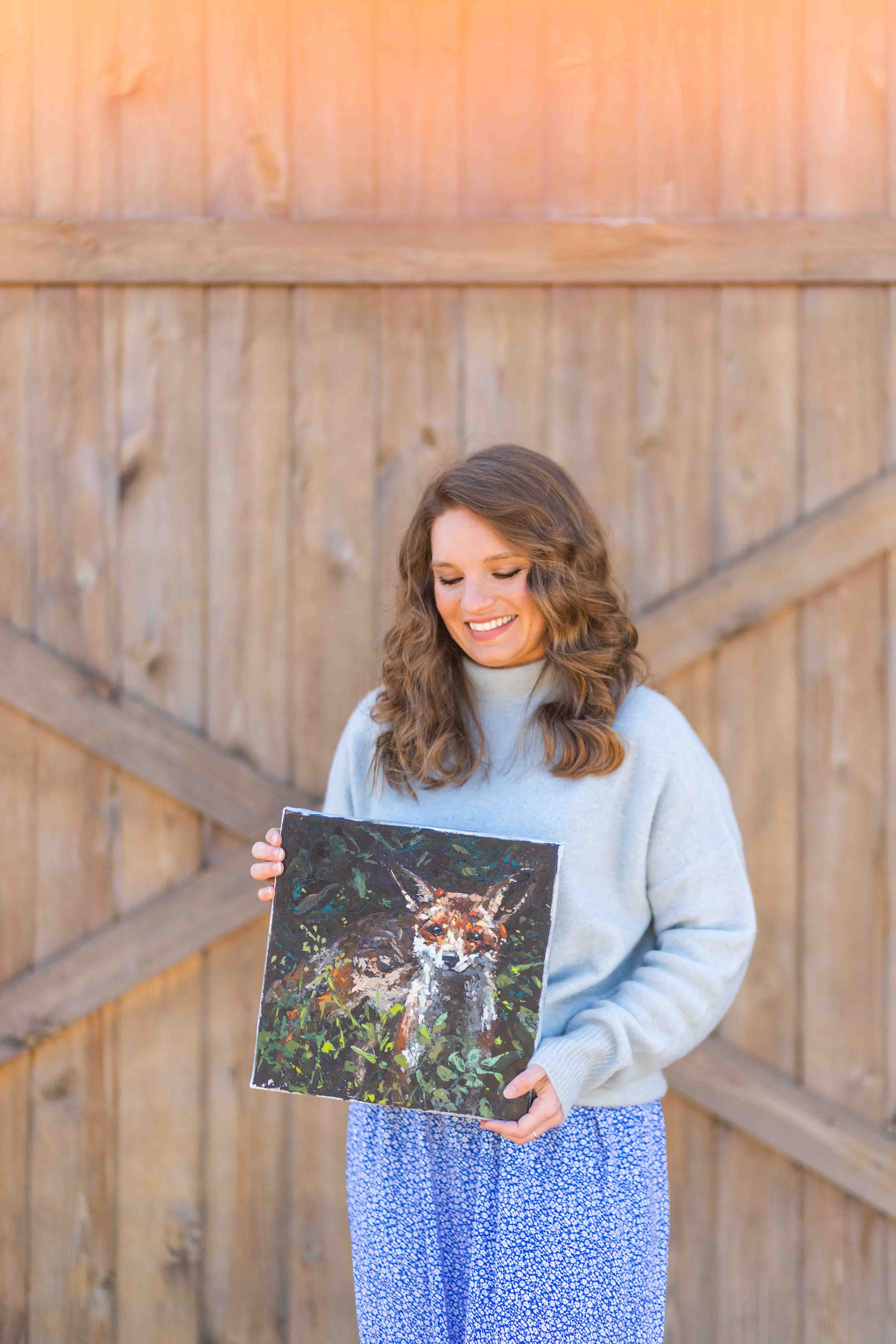 Artist Larissa Ann holding an original painting of a fox
