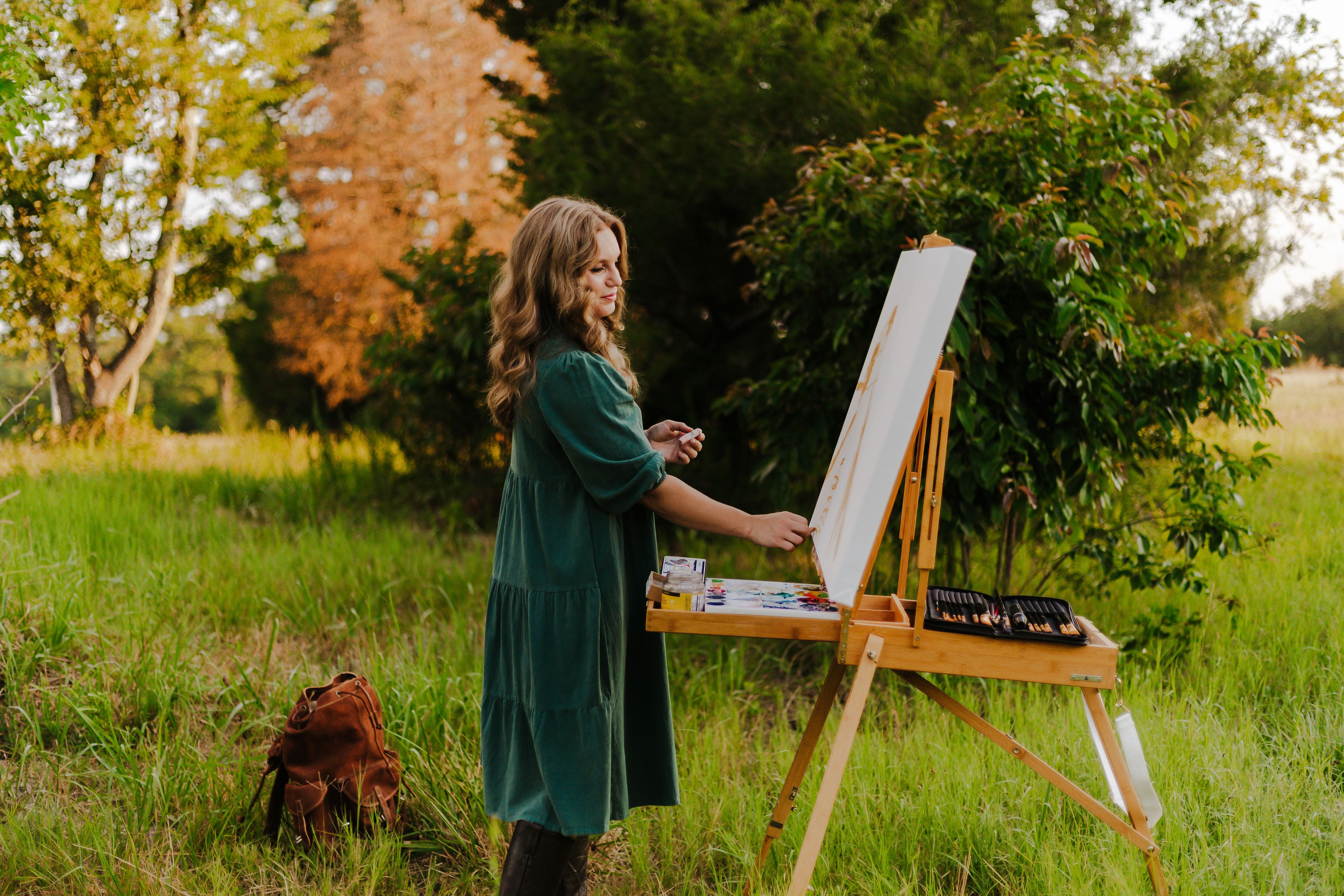 Equestrian artist Larissa Ann painting outdoors in a grassy field with trees in the background
