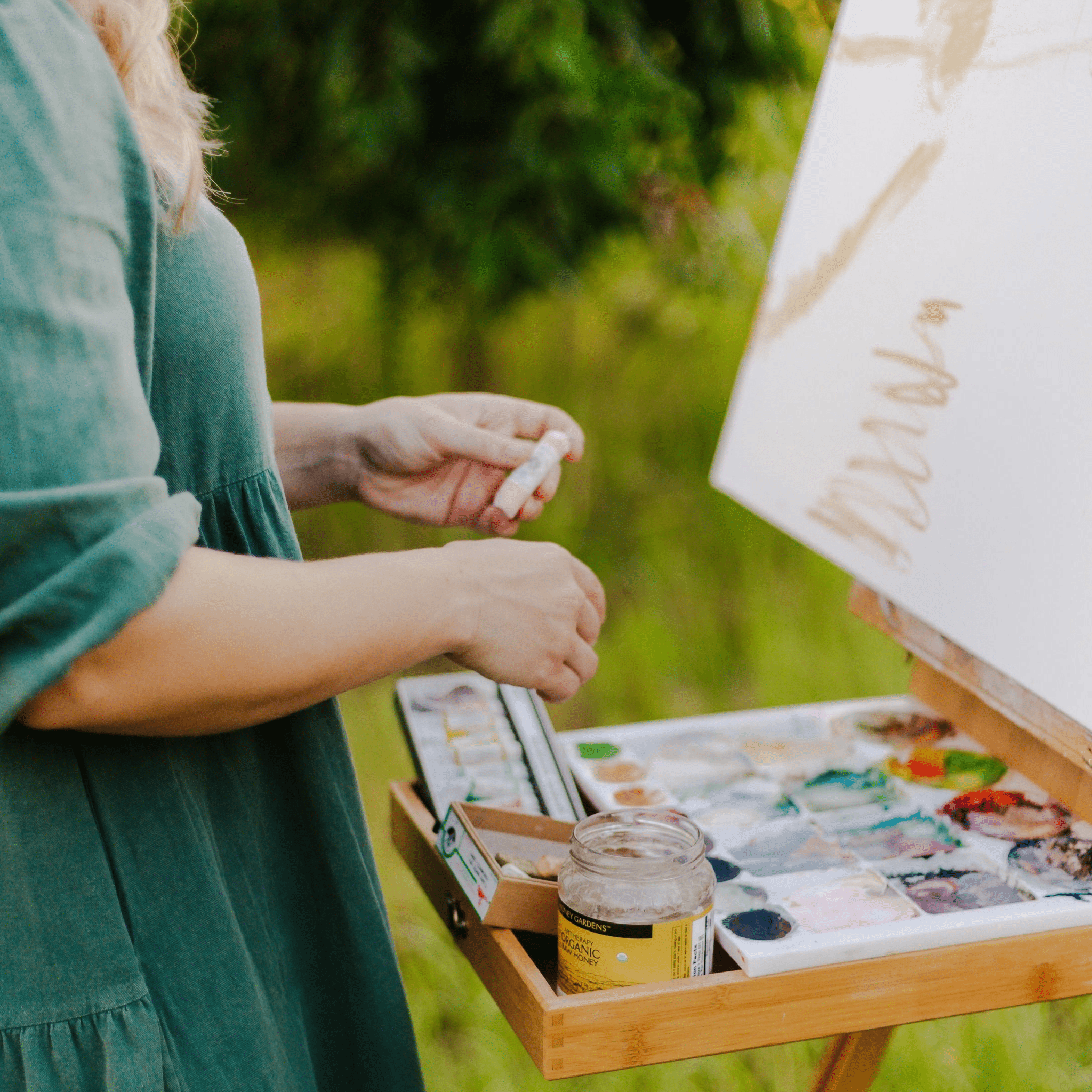 Equestrian artist Larissa Ann painting outdoors with a palette and paintbrushes on an easel.