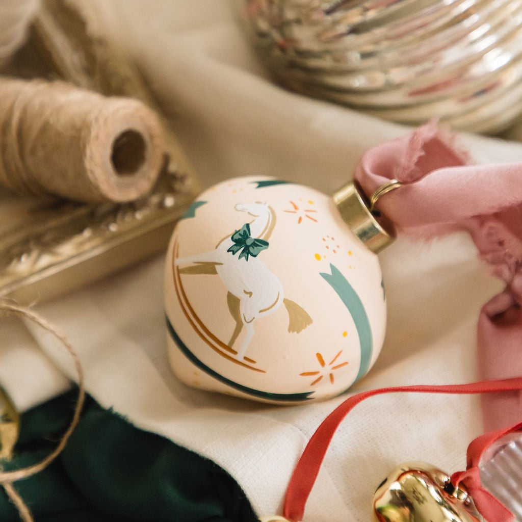 Decorative hand painted porcelain ornament with rocking horse design on a table with festive items.