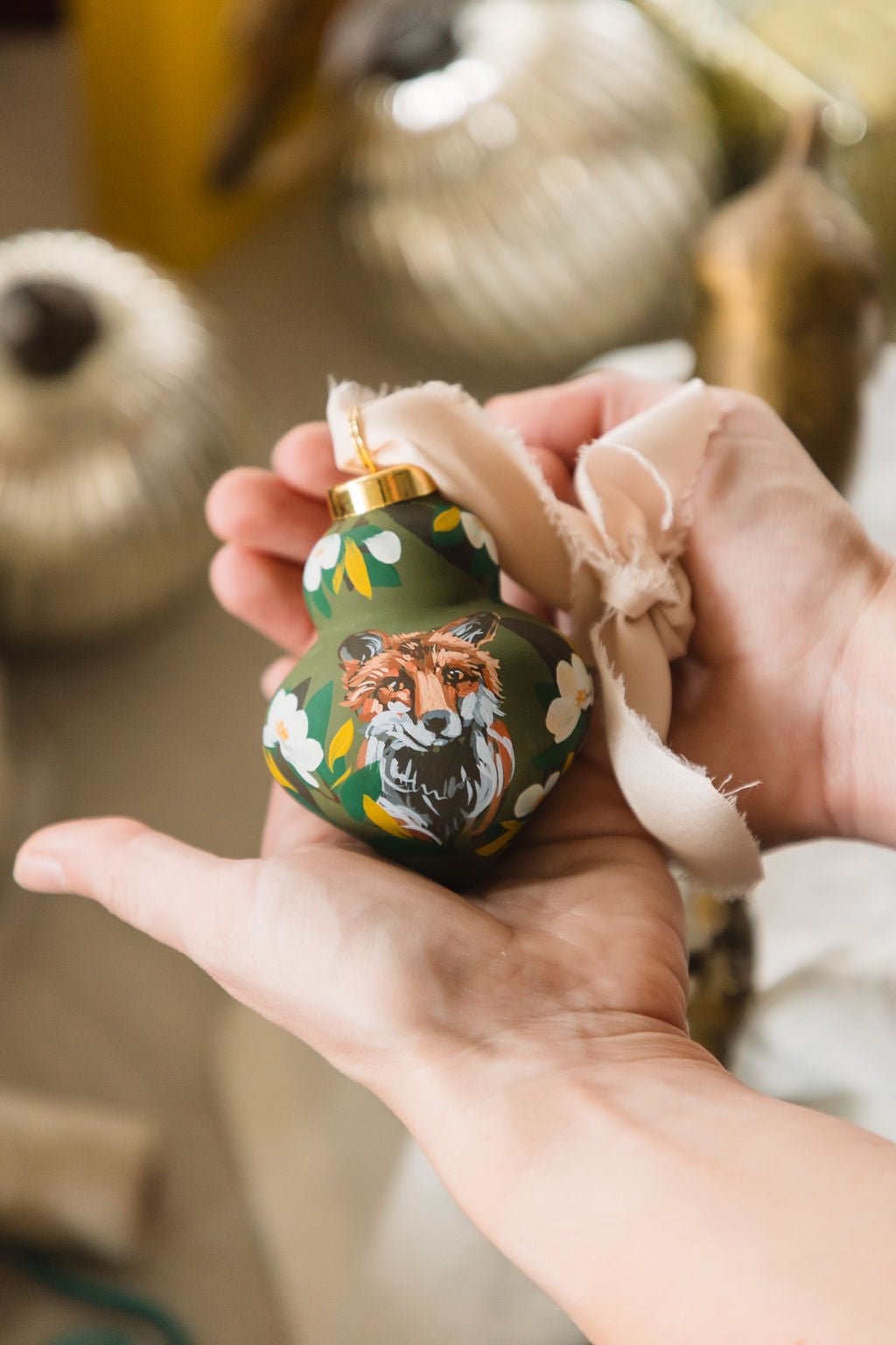 Hand holding a decorative ornament with a fox design against a blurred background