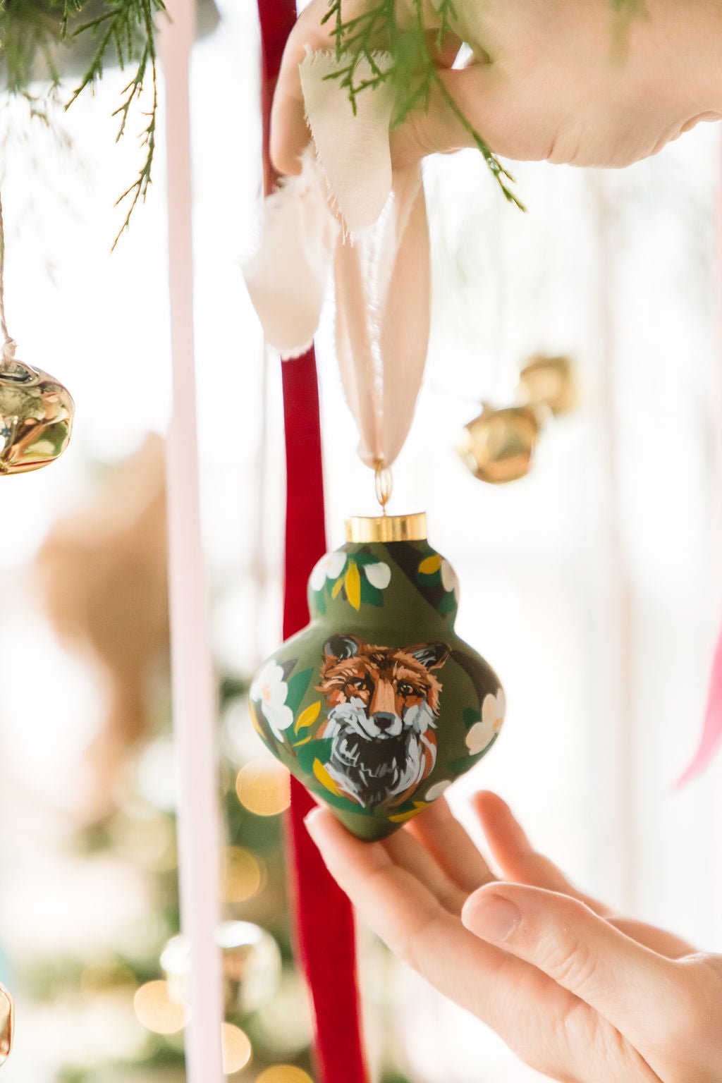 Hand holding a decorative Christmas ornament with a fox design against a festive background.