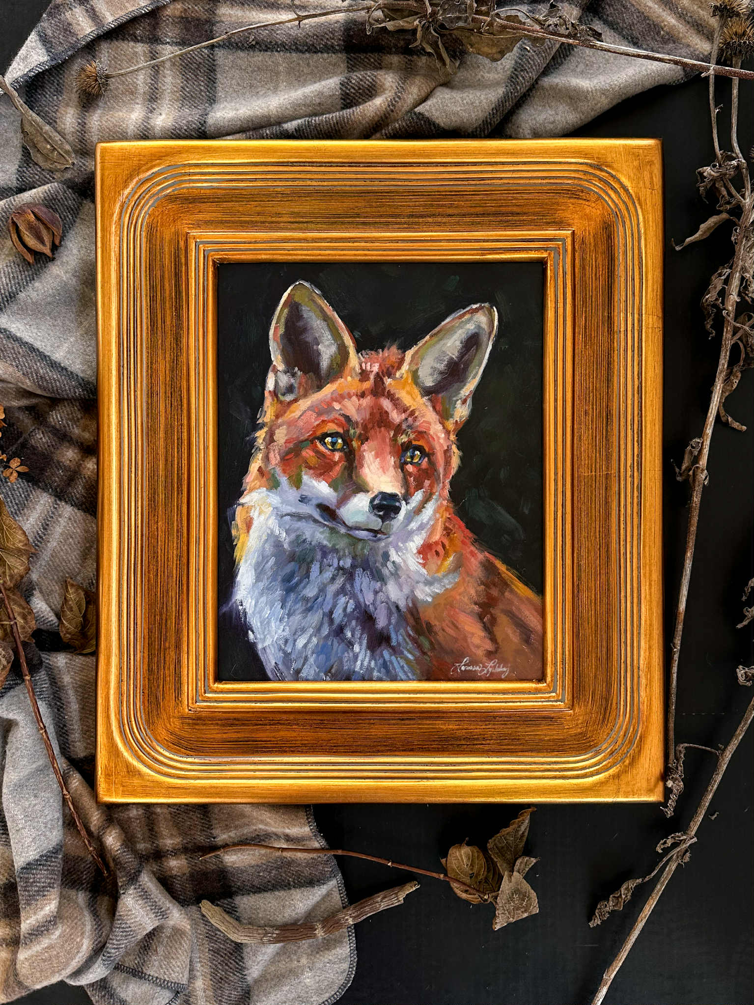 Framed painting of a fox on a dark background with a plaid fabric and branches.