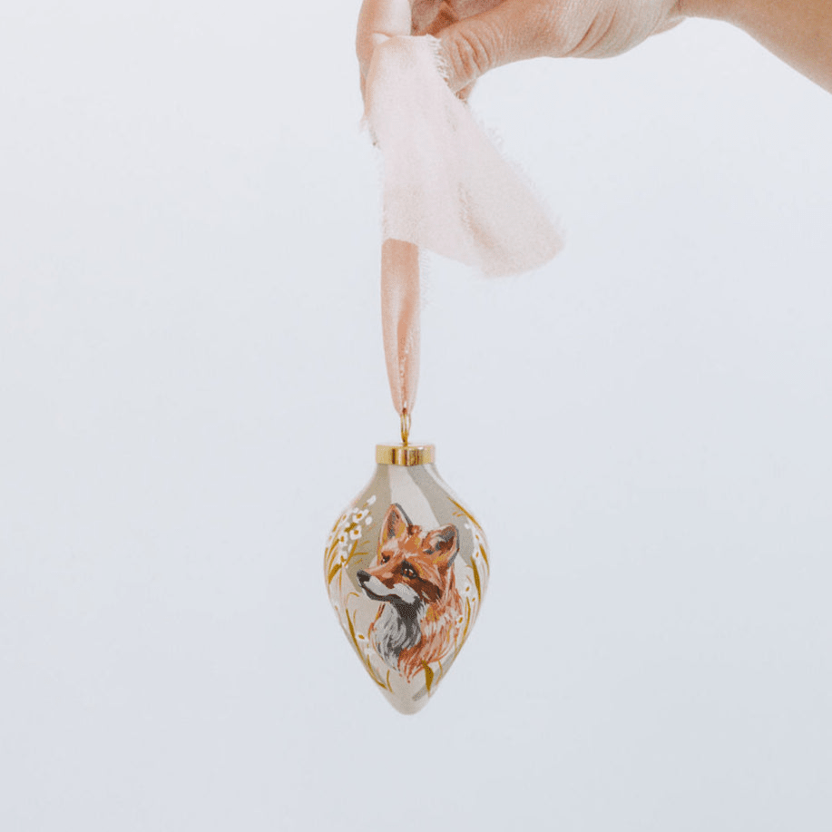 Decorative hand painted porcelain ornament with a fox design held by a hand against a white background