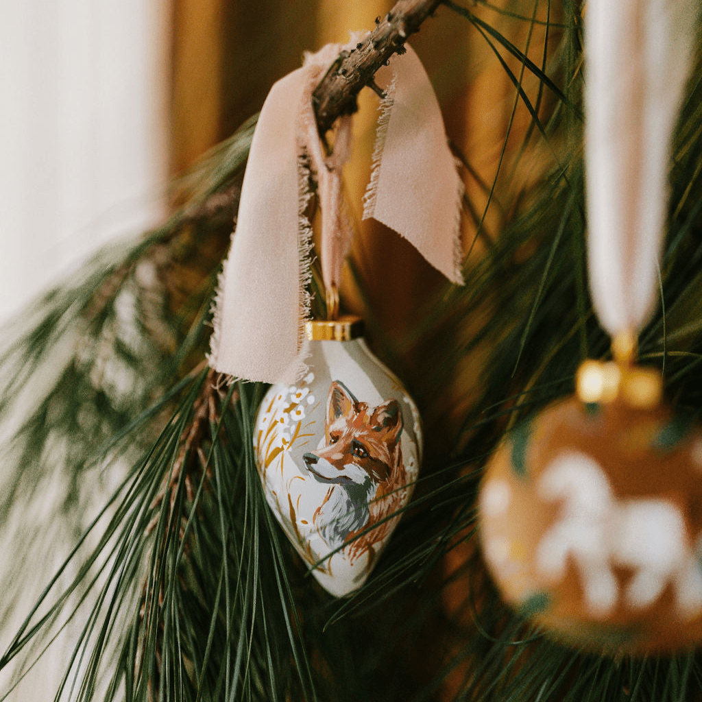 Decorative hand painted porcelain Christmas ornament with a fox design hanging on a branch.