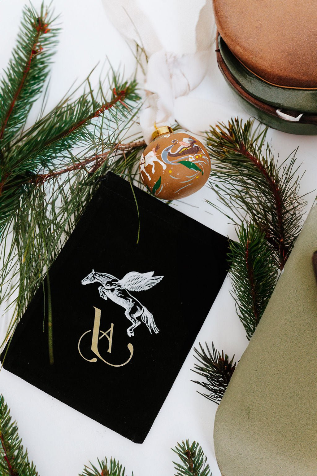 Black velvet gift bag with a white horse design surrounded by pine branches and a hand painted porcelain equestrian ornament.