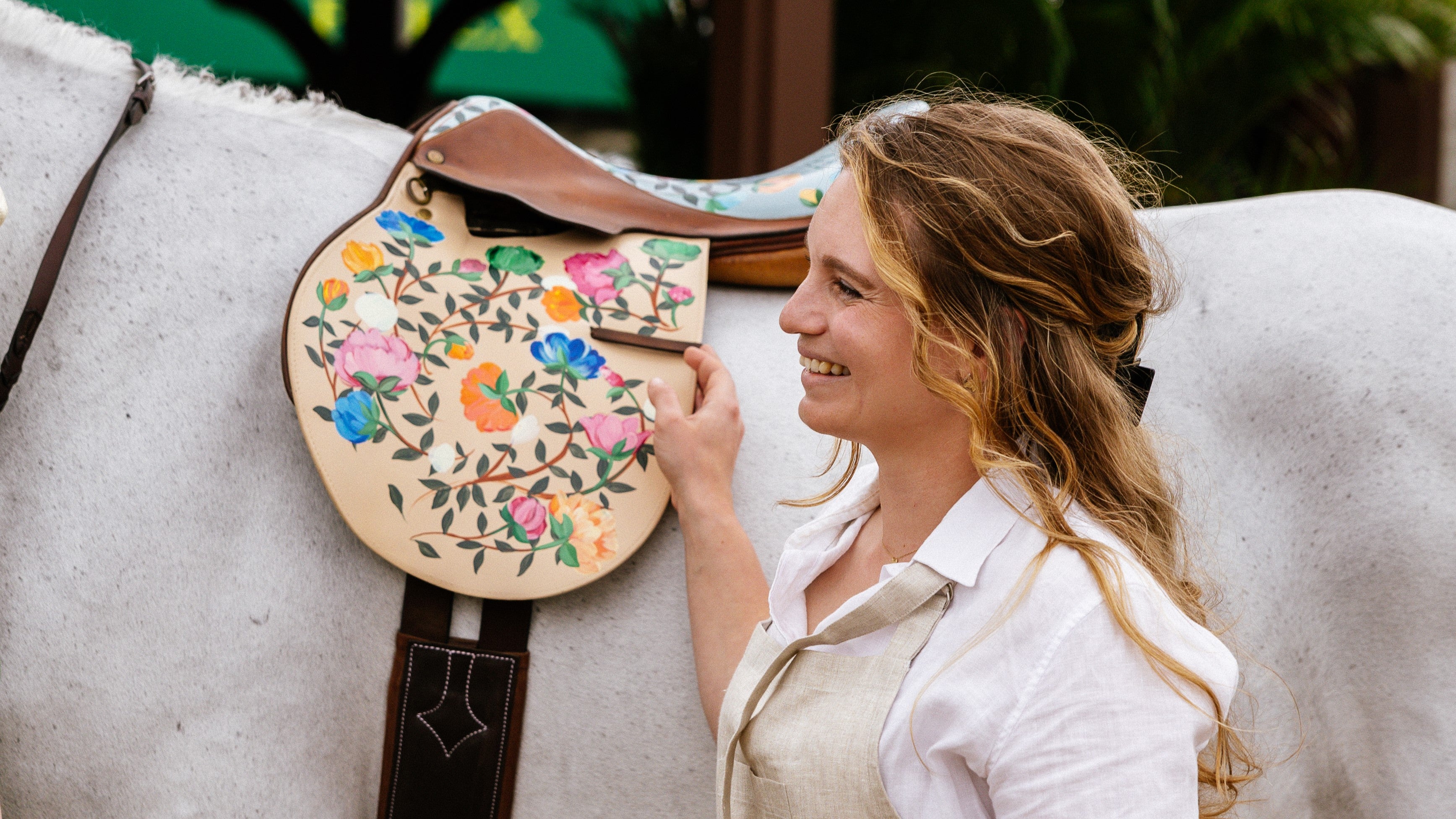Equestrian artist Larissa Ann holding a floral-painted saddle on a horse at Wellington