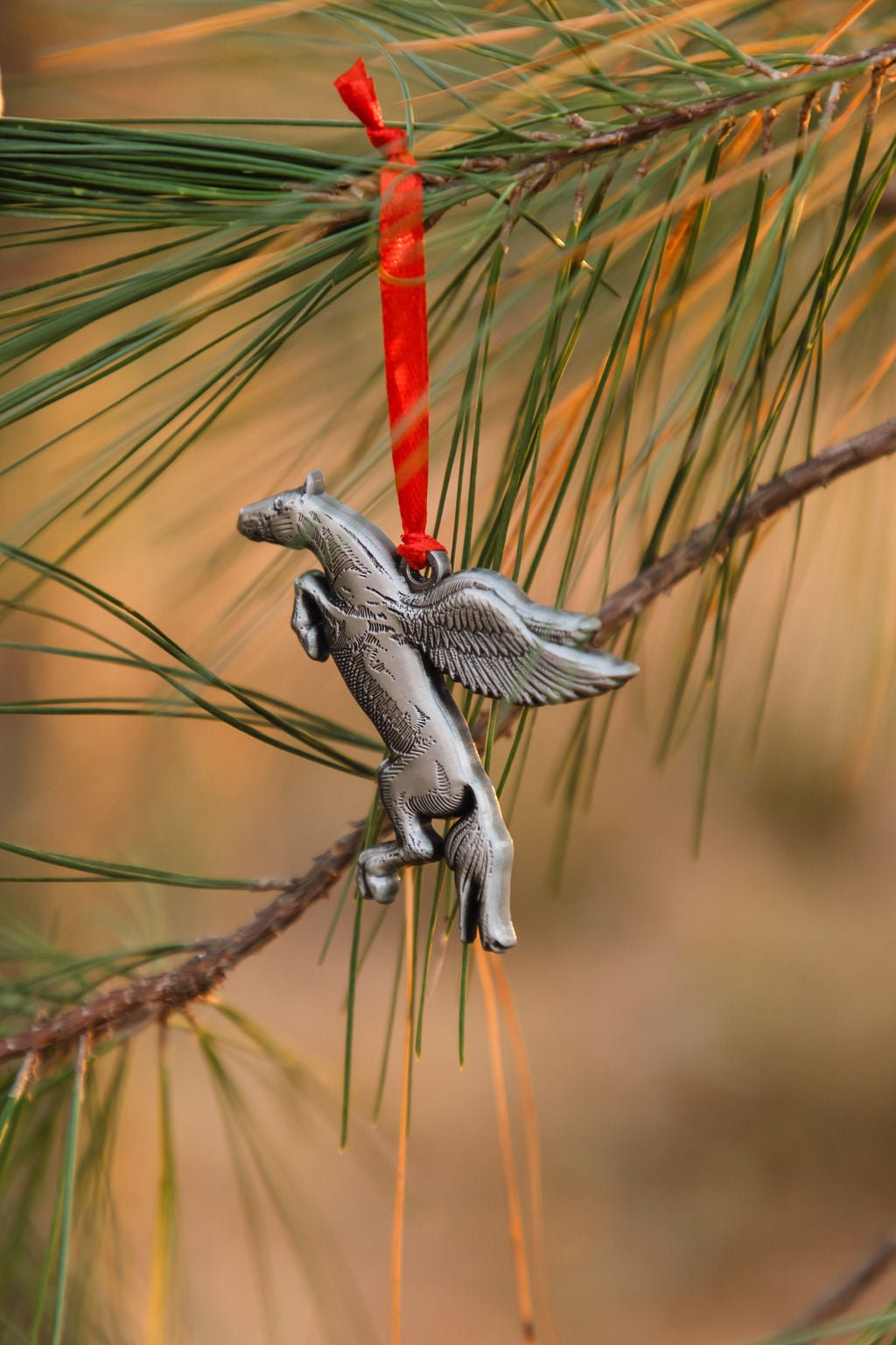 Decorative Pegasus ornament hanging on a pine branch with a red string.