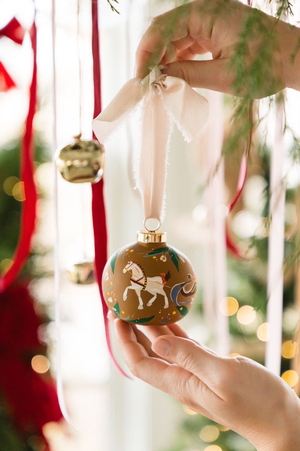 Hand holding a decorated Christmas ball ornament with a horse design, surrounded by festive decorations.