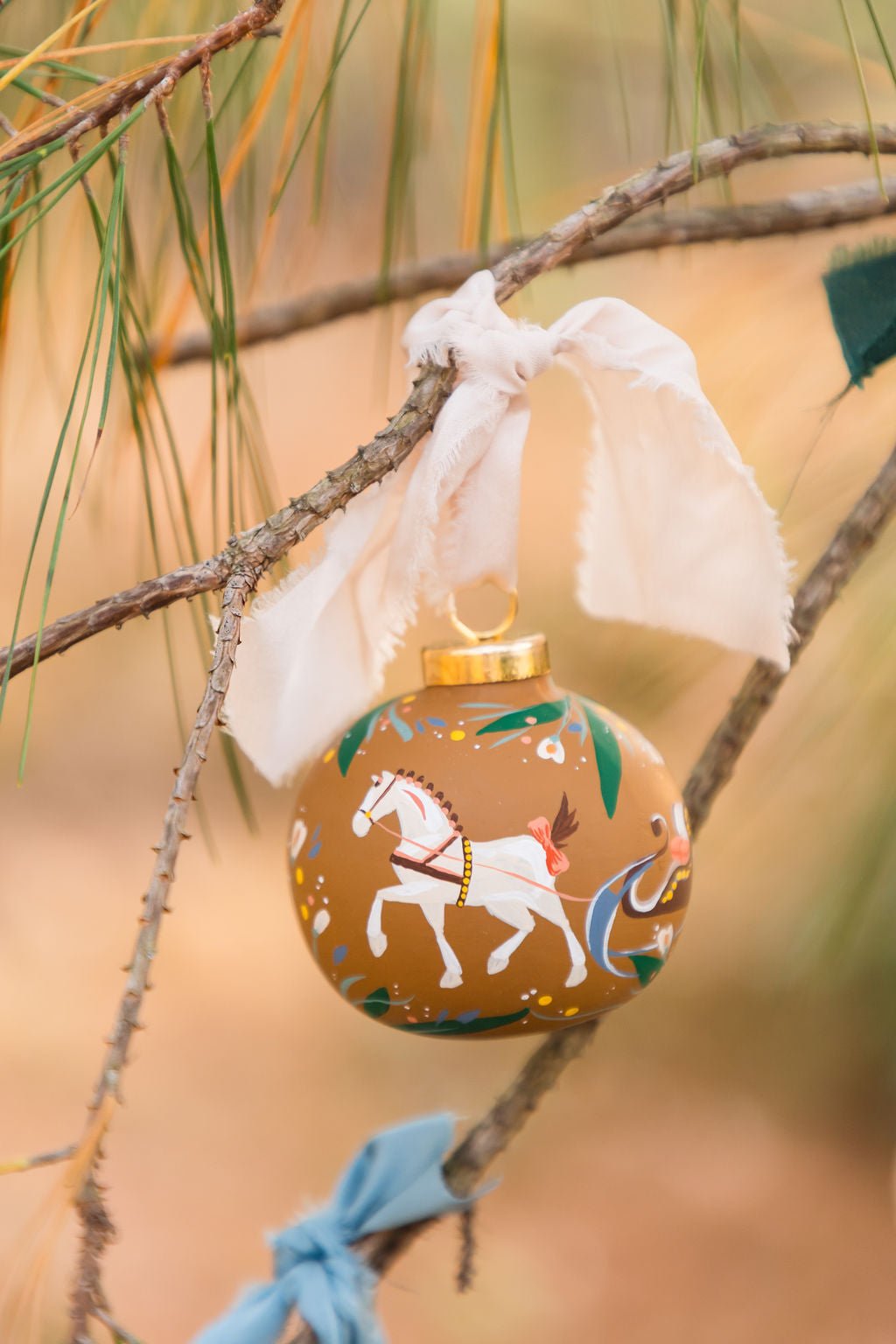 Decorative Christmas ornament with horse design hanging on a tree branch.