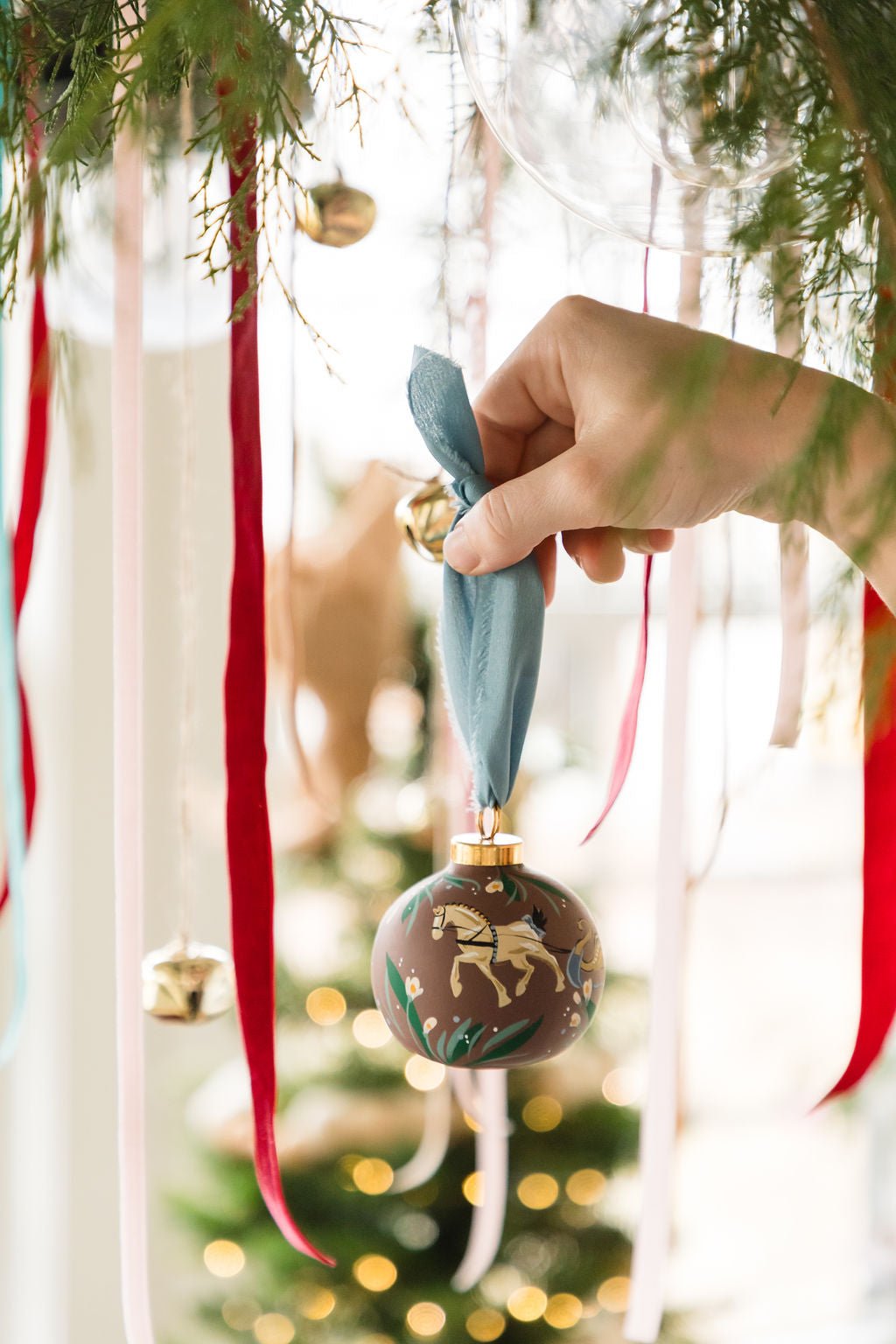 Hand holding a decorative Christmas ornament with a tree in the background