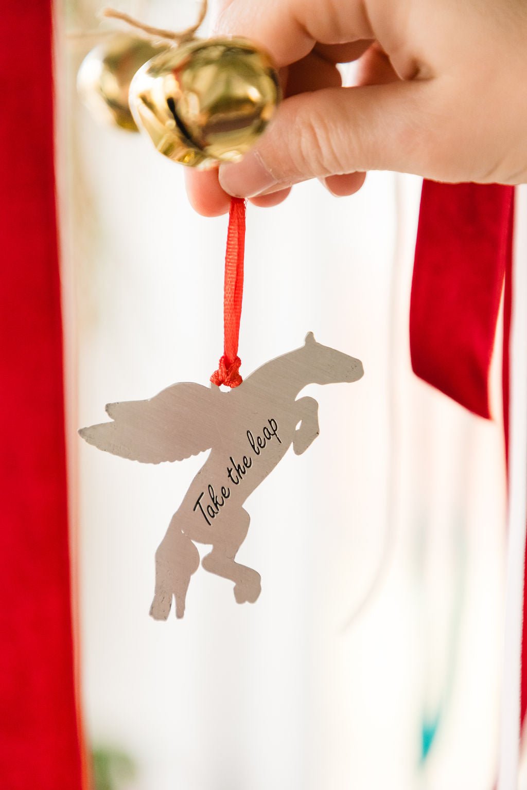 Decorative ornament with a horse silhouette and 'Take the leap' text, held by a hand against a red background.