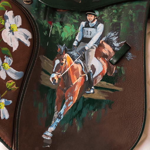 Decorative painted horse saddle with artistic designs featuring Will Coleman eventing his horse over cross country jump