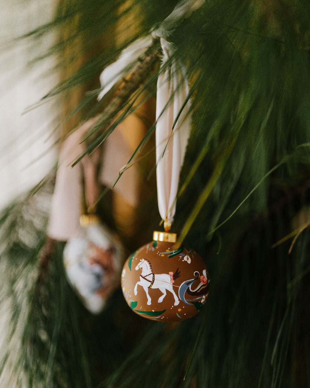 Hand painted porcelain decorative Christmas ornament with horse and sleigh design hanging on a tree