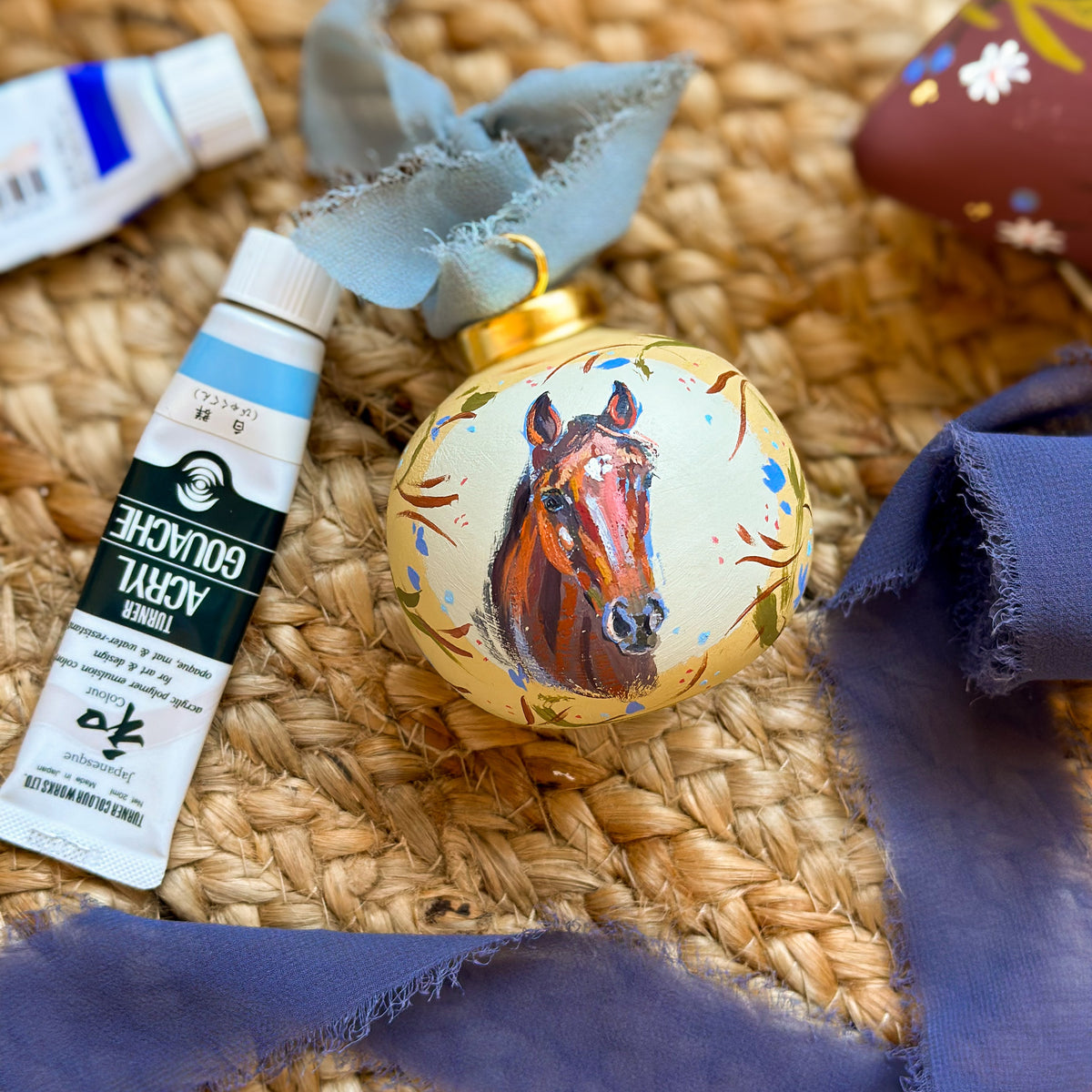 A custom hand-painted porcelain ornament featuring a brown horse head portrait on a cream background, decorated with blue and orange brushstrokes and tied with a dusty blue ribbon. Equestrian gifts, horse girl gifts, unique gift for someone who has everything