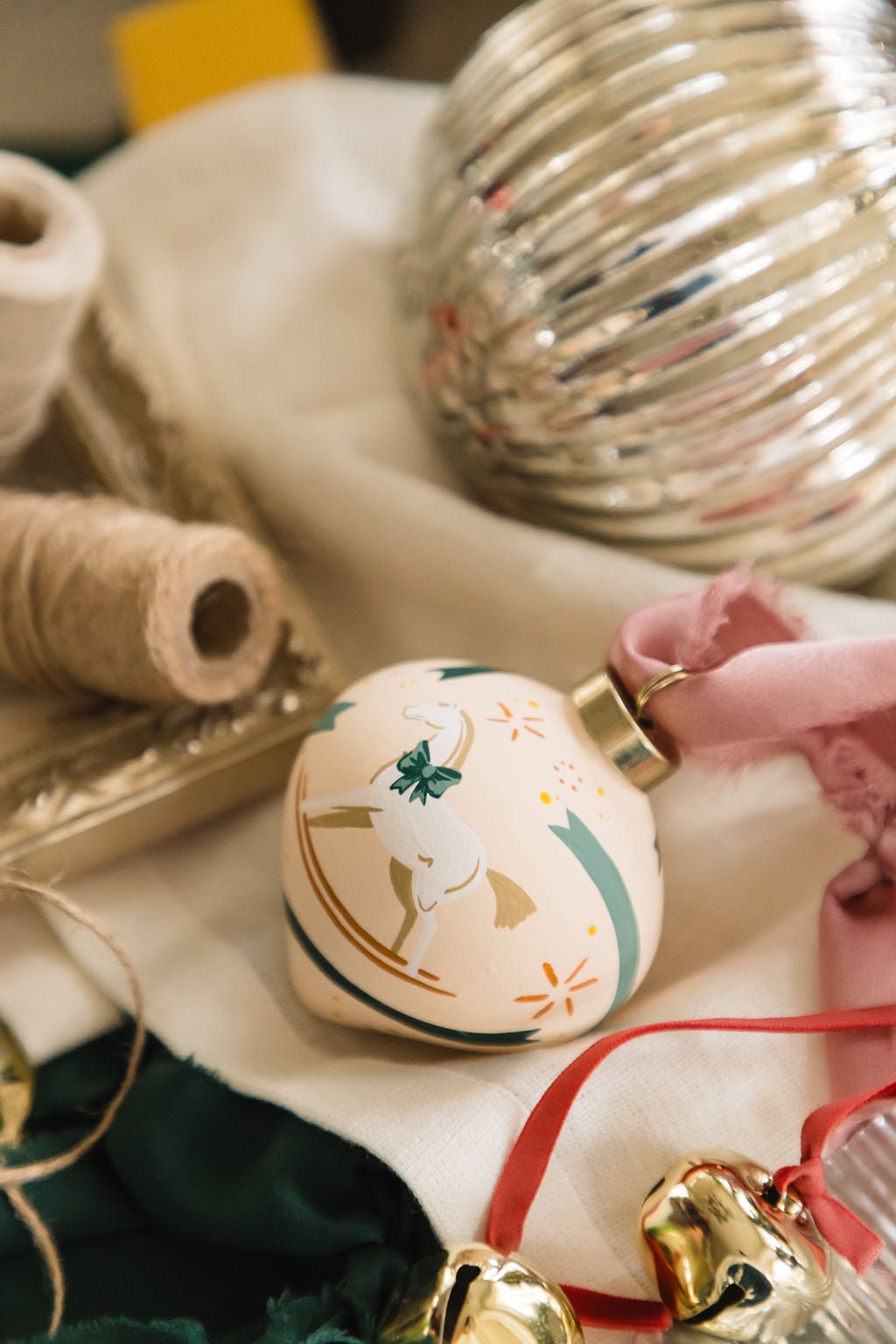 Decorative hand painted porcelain ornament with rocking horse design on a table with festive items.