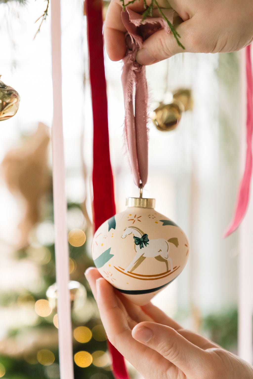 Hand painted decorative Christmas ball ornament with a rocking horse design, held by hands against a festive background.