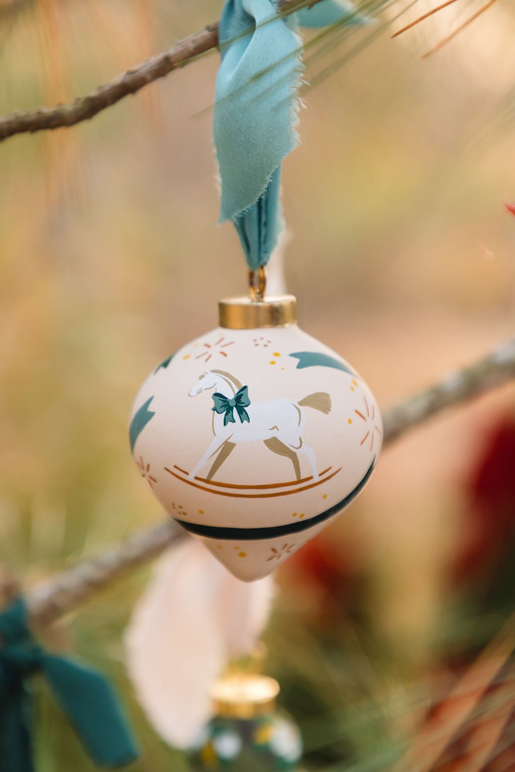 Decorative hand painted porcelain ornament with a horse design hanging on a branch