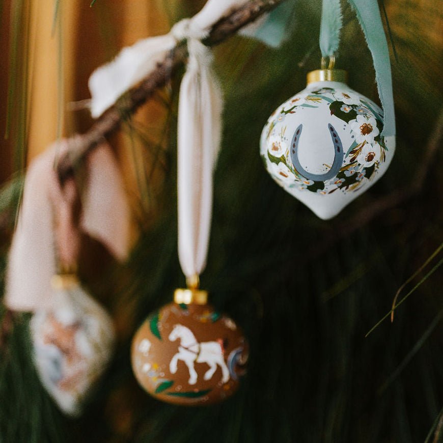 Decorative Christmas ornaments with horse designs hanging on a tree branch.