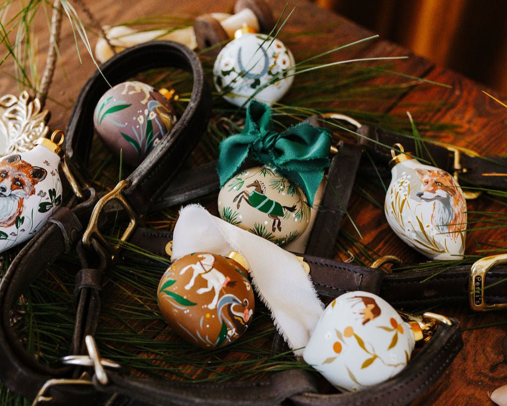 Decorative hand painted equestrian Christmas ornaments with silk ribbon on a wooden surface and greenery