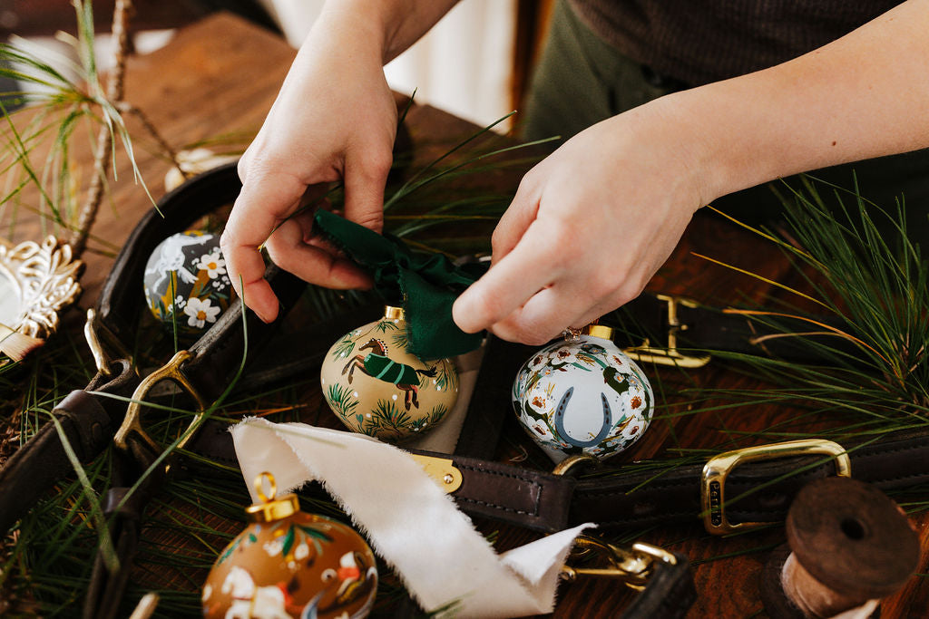 Equestrian artist Larissa Ann arranging decorative hand painted porcelain ornaments with horse designs on a surface with greenery