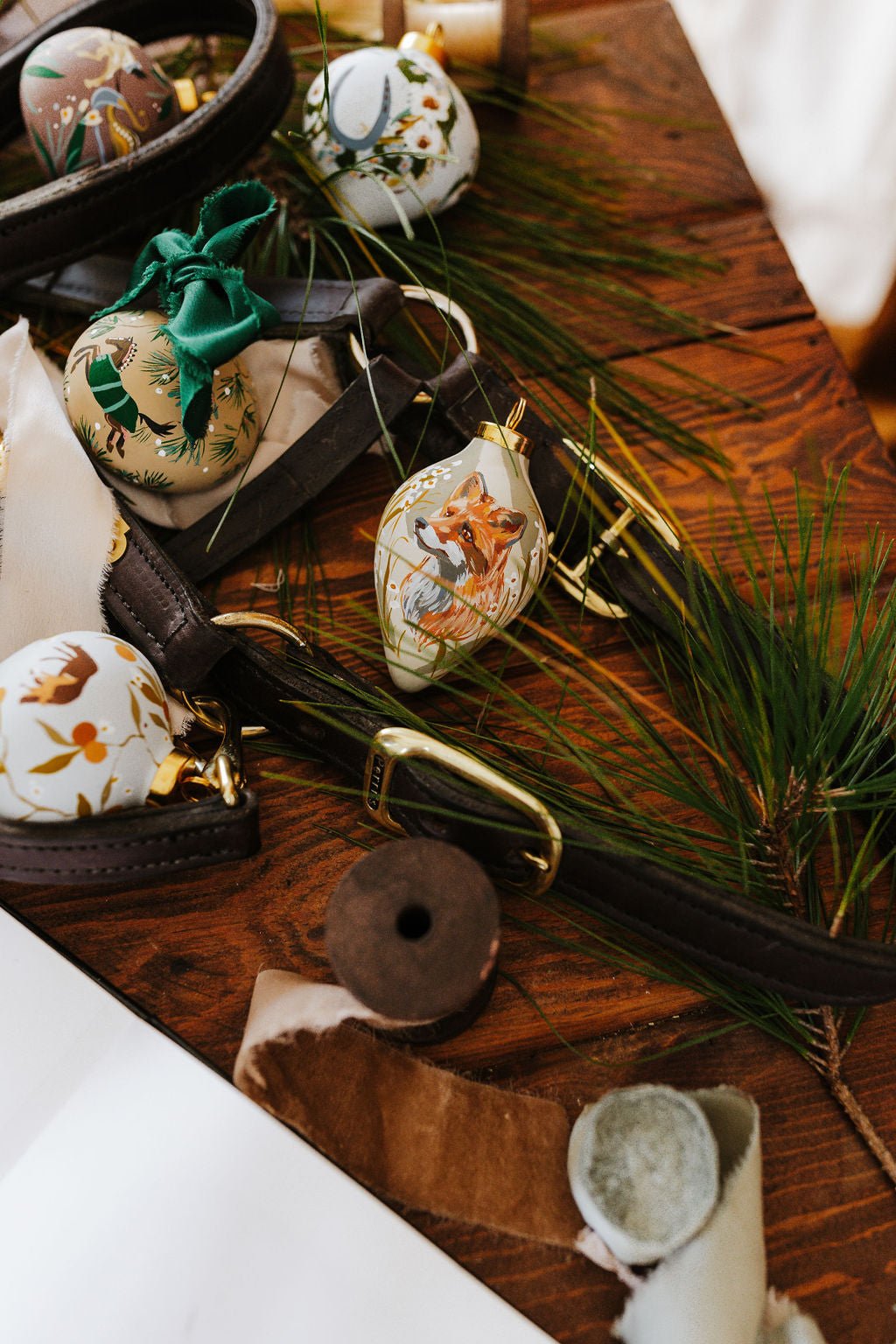 Decorative hand painted equestrian Christmas ornaments on a wooden surface with greenery