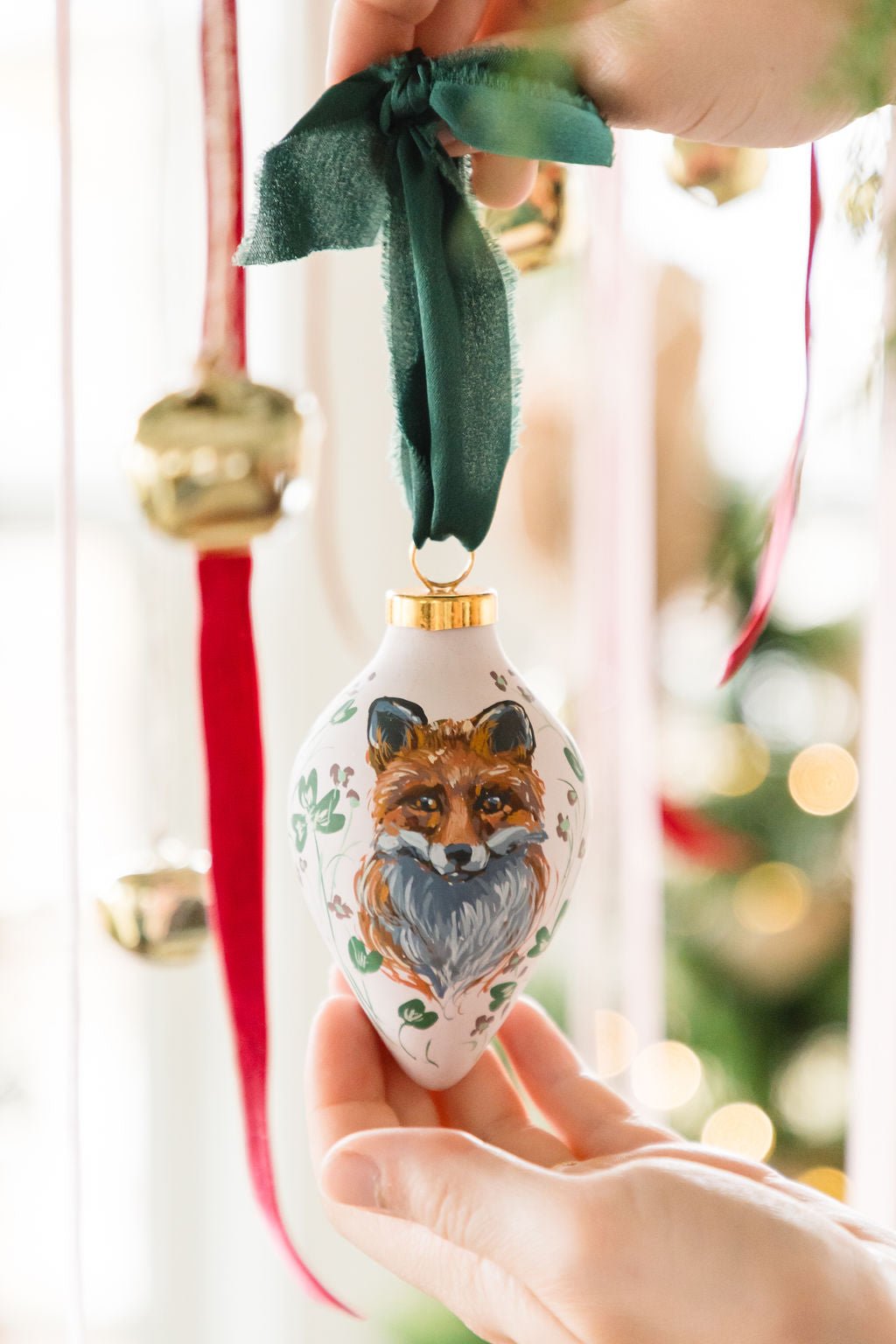 Hand painted decorative ornament with a fox design held by a hand against a blurred festive background.