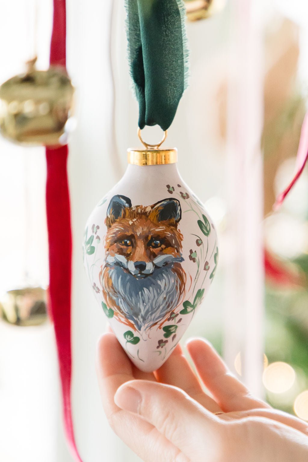 Hand holding a decorative hand painted fox ornament with a blurred festive background