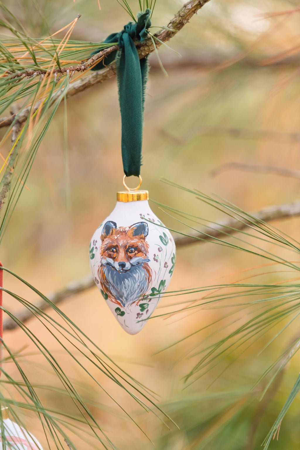 Hand painted decorative fox ornament hanging on a pine branch