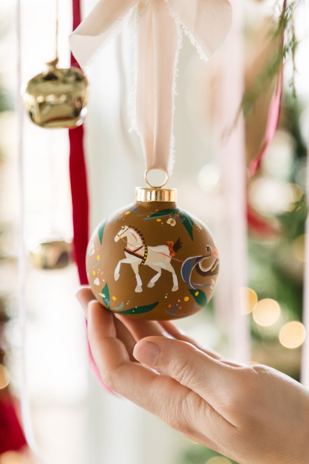 Hand holding a decorated Christmas ornament with a horse design against a festive background.