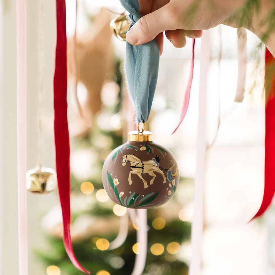 Hand holding a decorative Christmas ornament with a tree in the background