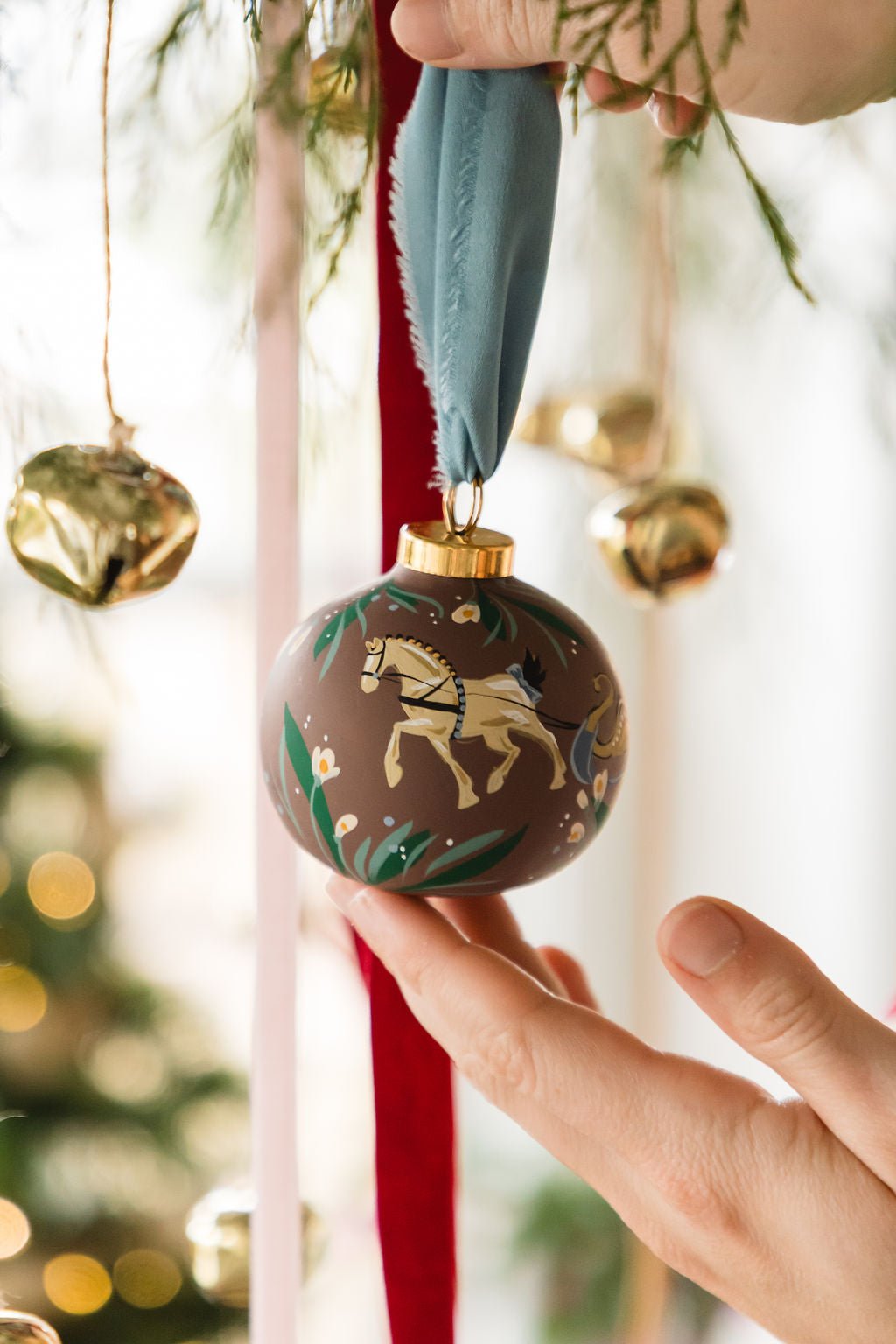 Decorative Christmas ornament with a horse design held by a hand against a festive background.