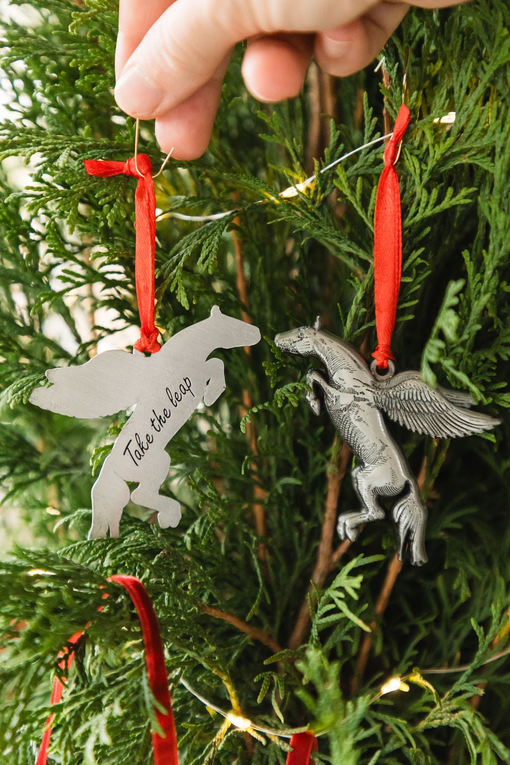 Decorative pegasus ornaments with red ribbons hanging on a Christmas tree.