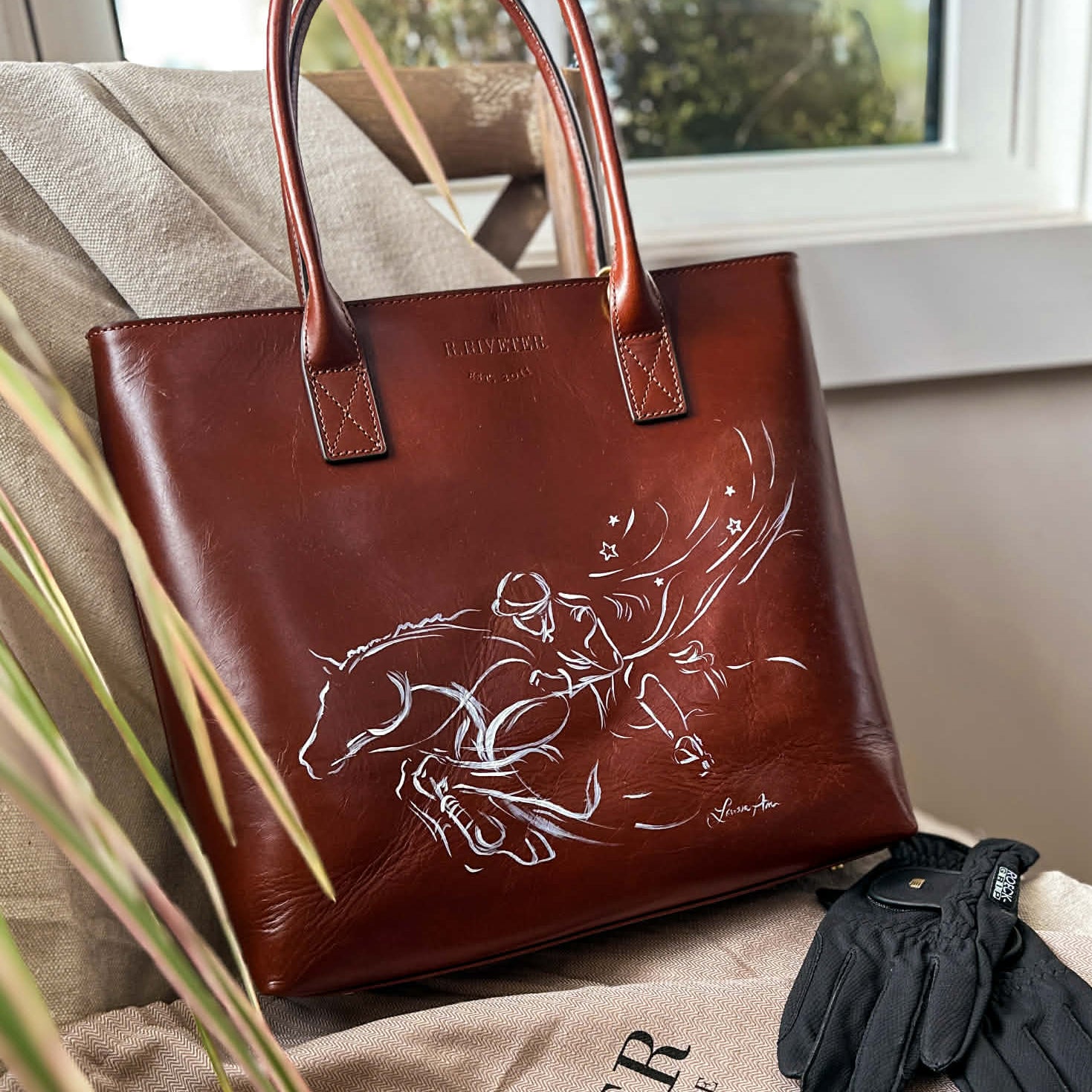 A custom painted leather tote bag with an equestrian design by artist Larissa Ann