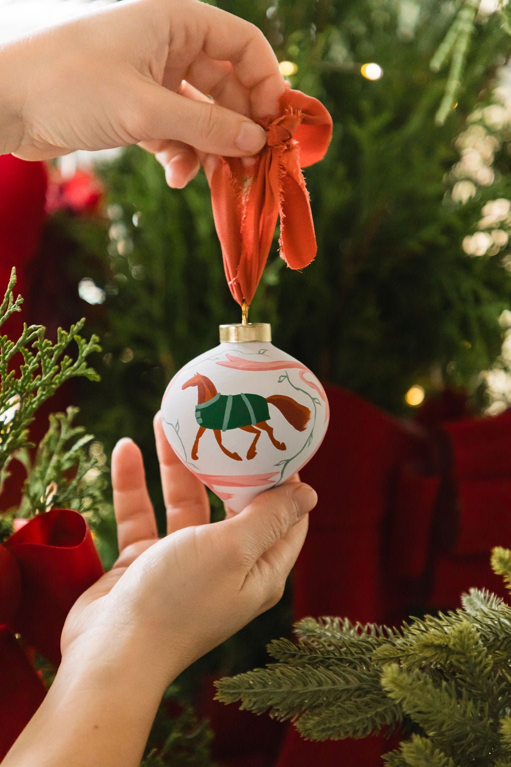 Hand holding a Christmas ornament with horse design against a festive background