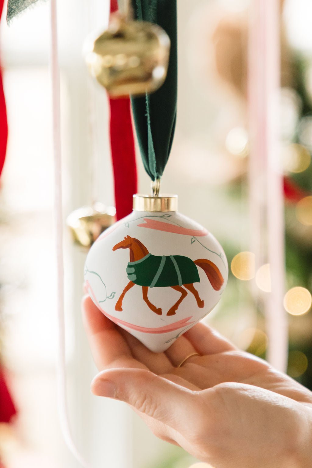 Hand holding a Christmas ornament with a horse design against a festive background